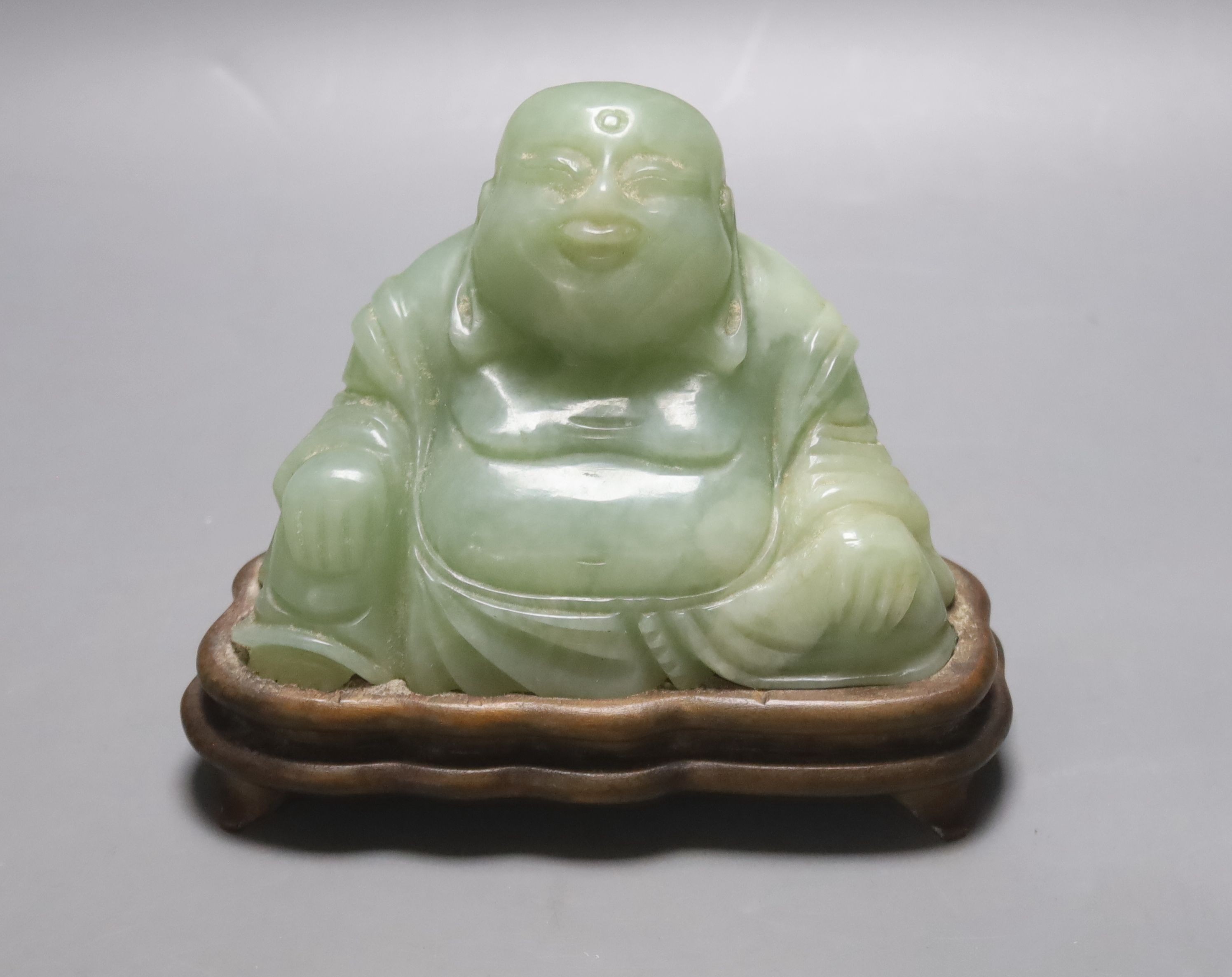 A Chinese carved bowenite jade figure of a seated Budai, H 9cm, W 13cm on carved wooden stand